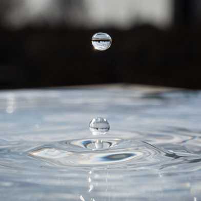 A drop of water hits the water surface and causes movement in the water. 