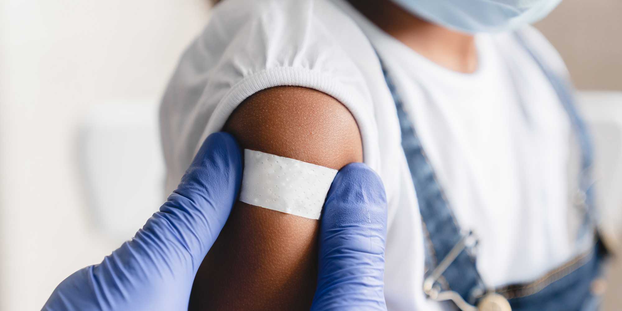 Close-up of a nurse applying a medical patch to a little girl after vaccination.